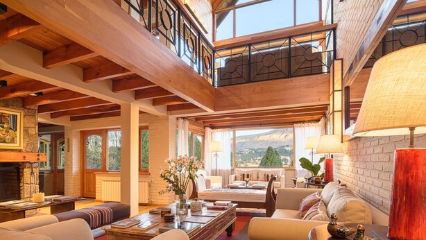 A spacious living area with a high ceiling, wooden beams, and large windows offering a mountain view. - Casona del Alto (San Martín de los Andes)