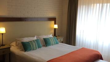 Ein Hotelzimmer mit einem großen Bett, zwei Nachttischlampen, einem Kopfteil, einer Bank, einem Nachttisch und einem fenster mit Vorhängen.