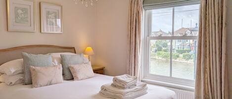 A neatly made bed with pillows, a chandelier, a lamp, and a view of a canal through a window.