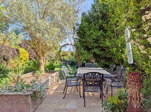 Een terras buiten, met een tafel en stoelen, omringd door verschillende planten en bomen.