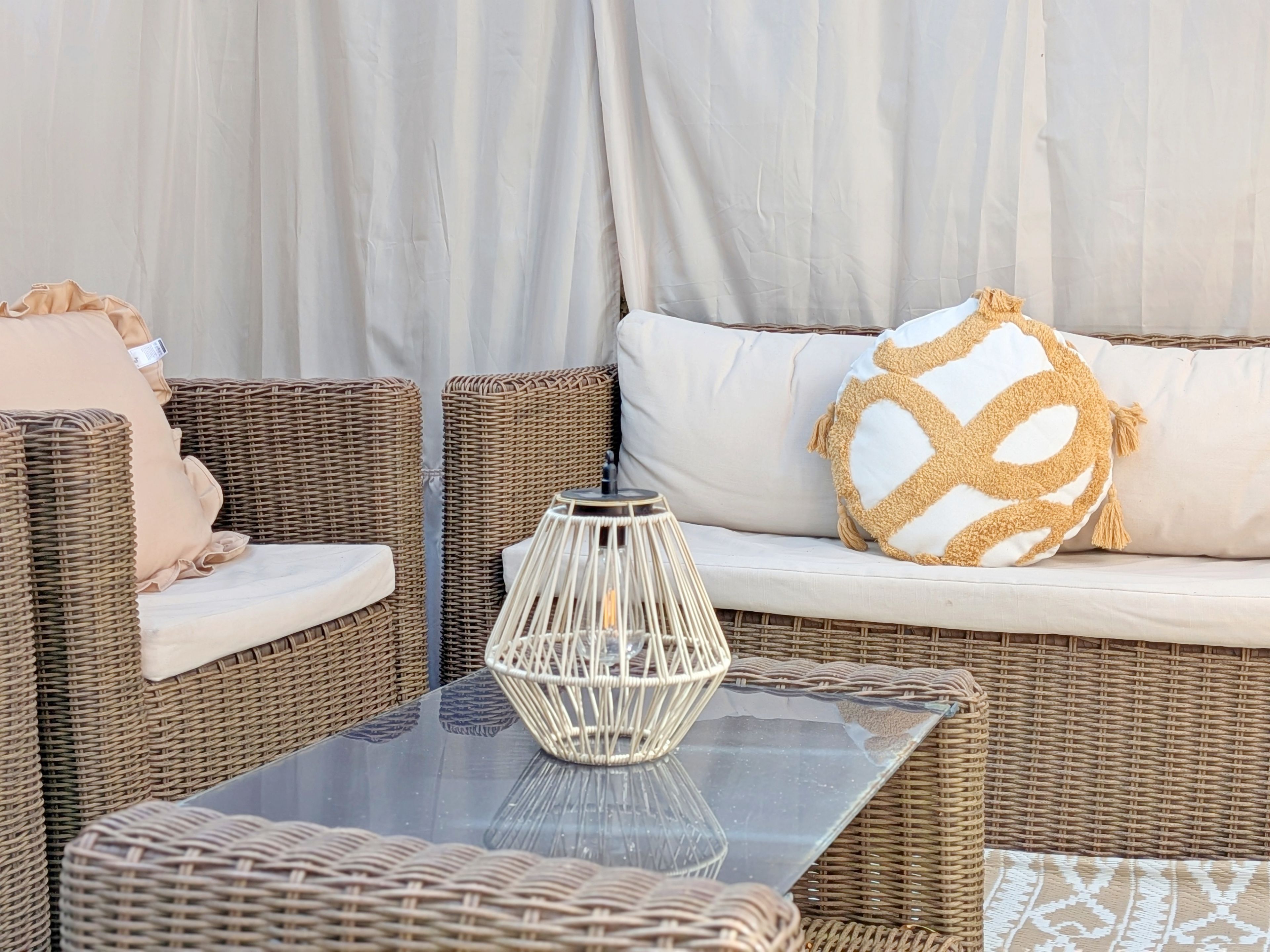 A wicker sofa with cushions, a glass-top table, and a decorative vase.