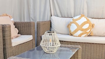 A wicker sofa with cushions, a glass-top table, and a decorative vase.