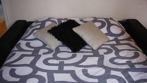 A bed with a patterned bedspread and two pillows, one black and one beige. - Apartment TOU T CONFORT, in the HEART of Old Lille, Balconnet (Lille)