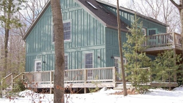 Een ruime, houten chalet met twee verdiepingen en een balkon, omringd door bomen en sneeuw.