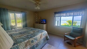 Un dormitorio con cama, televisor, silla y ventana con vista al océano.
