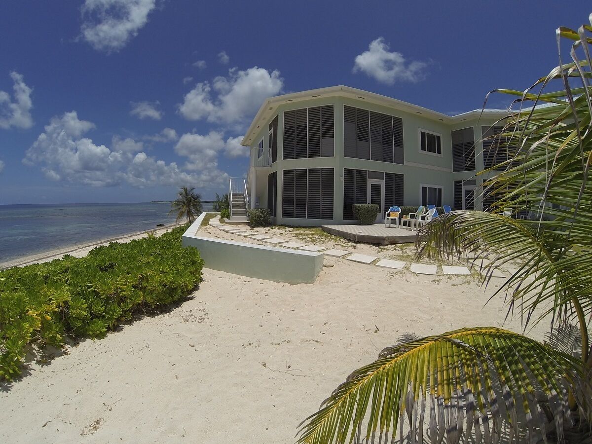 A beachfront property with a modern house, a sandy beach, and palm trees.