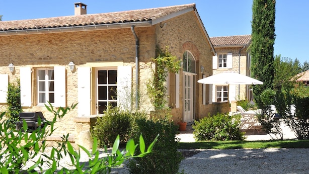 A stone building with a tiled roof, a covered patio with a white umbrella, and a gravel driveway. - Le Colombier, 10p., at the beautiful “Domaine de Vincenti” (Domaine de Vincenti Divajeu)