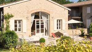 A stone building with a large arched doorway, a balcony, and a patio area with outdoor furniture. - Le Colombier, 10p., at the beautiful “Domaine de Vincenti” (Domaine de Vincenti Divajeu)