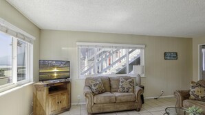 A living room with a sofa, a wooden cabinet, a television, and a large window with a view of buildings and a staircase.