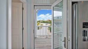 Blick von einem Balkon mit Holzboden, einer Glastür und einem Edelstahlkühlschrank.