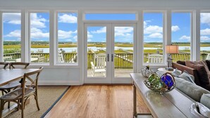 Ein geräumiges Zimmer mit großen Fenstern und Blick auf einen Wasserweg. Es gibt einen Essbereich mit Tisch und Stühlen sowie eine Sitzecke mit einer Couch und dekorativen Elementen.