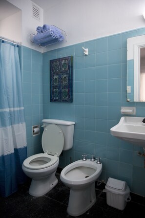 A bathroom with two toilets, a bidet, a sink, a shower curtain, and a decorative tile wall. - Comfortable Apartment in Palermo (Buenos Aires)