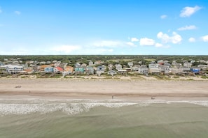 Uma área residencial costeira com casas ao longo da praia, uma praia de areia e céu claro.