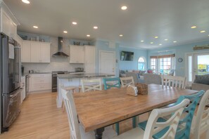 Une cuisine avec des meubles blancs, une table à manger en bois et des chaises de couleur turquoise.