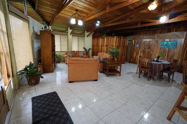A spacious room with a wooden ceiling, a sofa, a dining table with chairs, and a potted plant.