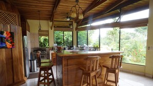 Cozinha com banquetas de madeira, uma ilha grande e vista para o verde através de amplas janelas.