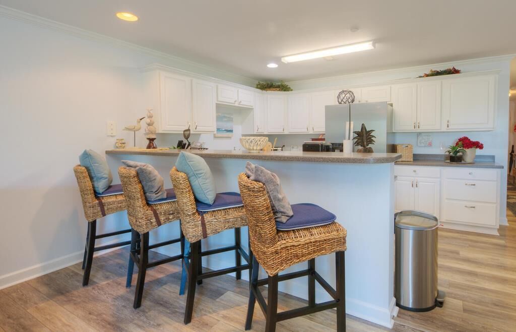 A kitchen with white cabinets, a stainless steel refrigerator, and a bar area with wicker chairs.