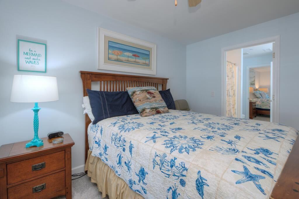 A bedroom with a bed, a nightstand, a lamp, a framed picture, and a door leading to another room.