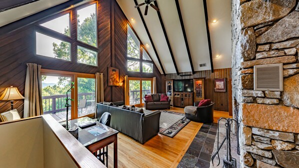 A spacious living area with a wooden ceiling, stone walls, and large windows offering a view of the outdoors.