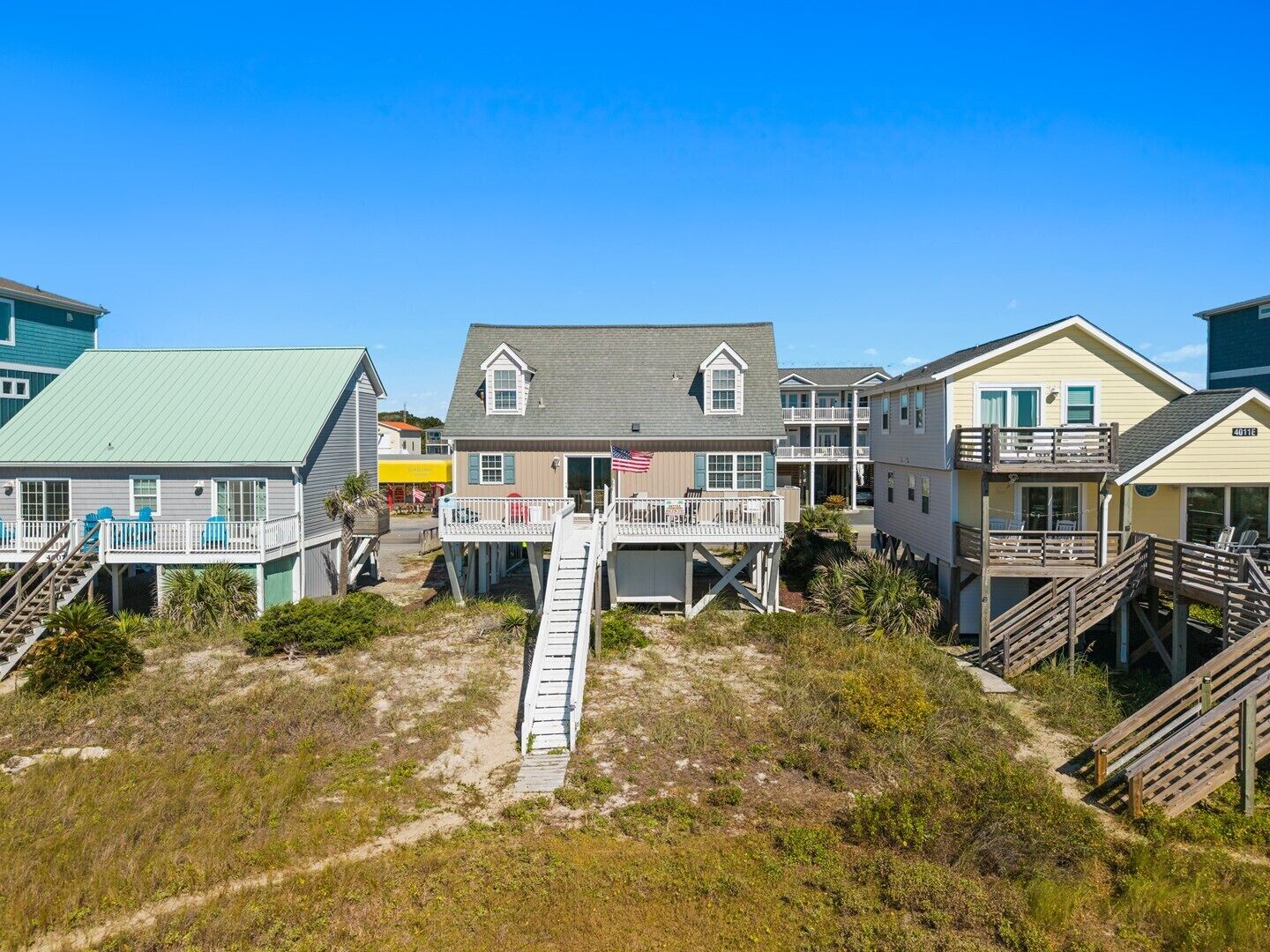 Een strandpand met meerdere gebouwen, waaronder een huis met terras en vlag, en een gebouw met balkon.