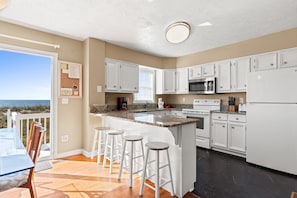 A modern kitchen with white cabinets, a granite countertop, and a large island with bar stools.