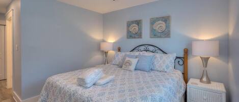 A bedroom with a bed, two wall-mounted lamps, a ceiling fan, and two framed artworks on the wall.