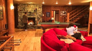 Una habitación acogedora con chimenea de piedra, mesa de billar y sofá rojo.