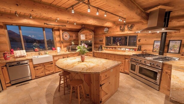 Una cocina amplia con armarios de madera, una isla central con taburetes, una estufa grande y vistas a un lago a través de las ventanas.