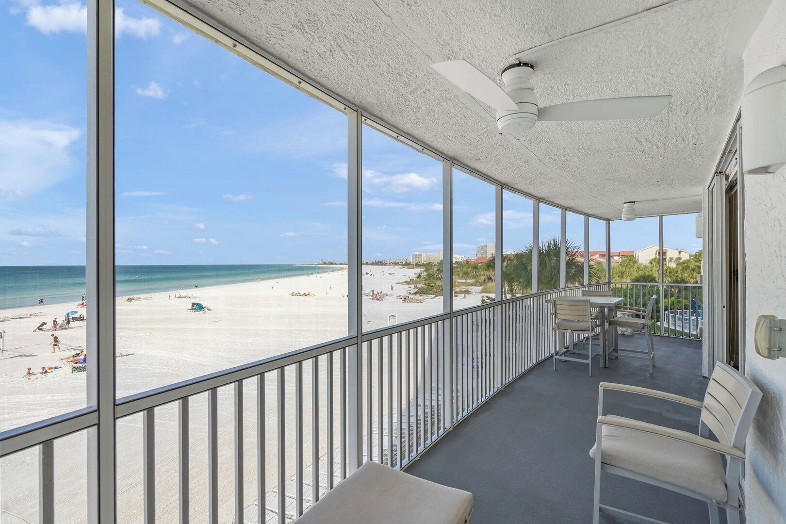 Un balcon avec vue sur la plage, un ventilateur de plafond et une table avec des chaises.