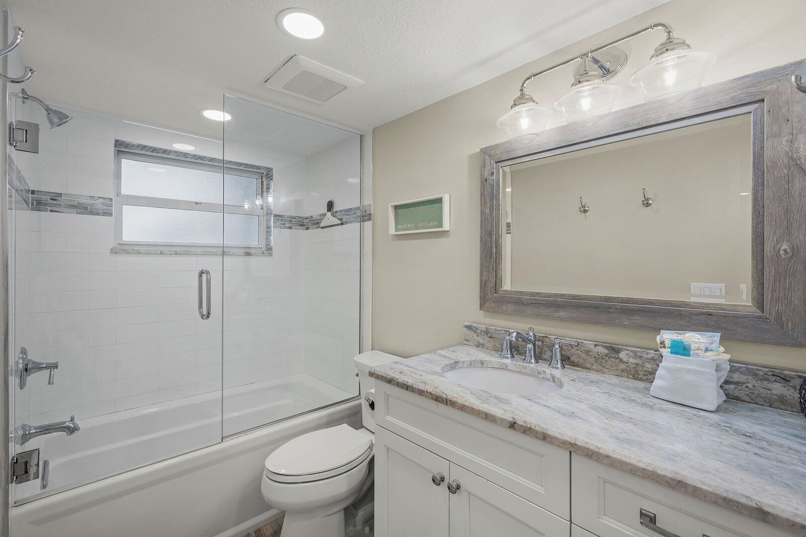 Une salle de bain dotée d’une douche à parois de verre, de toilettes, d’un lavabo avec un plan de travail en marbre et d’un grand miroir au-dessus du lavabo.