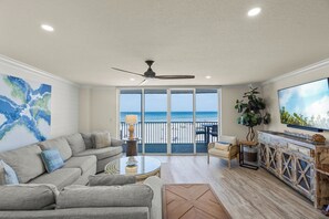 A spacious living room with a large sofa, a coffee table, and a TV. There is a balcony with a view of the ocean. - Crystal Sands Tower Unit 304 - Beachfront (Sarasota)