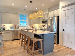 A modern kitchen with a central island, stainless steel appliances, and wicker pendant lighting.