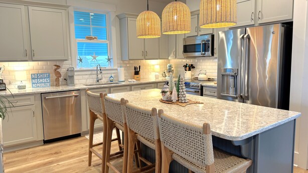 A modern kitchen with a central island, stainless steel appliances, wicker chairs, and pendant lighting. - A Toast at the Coast: Luxury oceanview home in Oak Island, featuring 5 kings, private heated pool. (Oak Island)