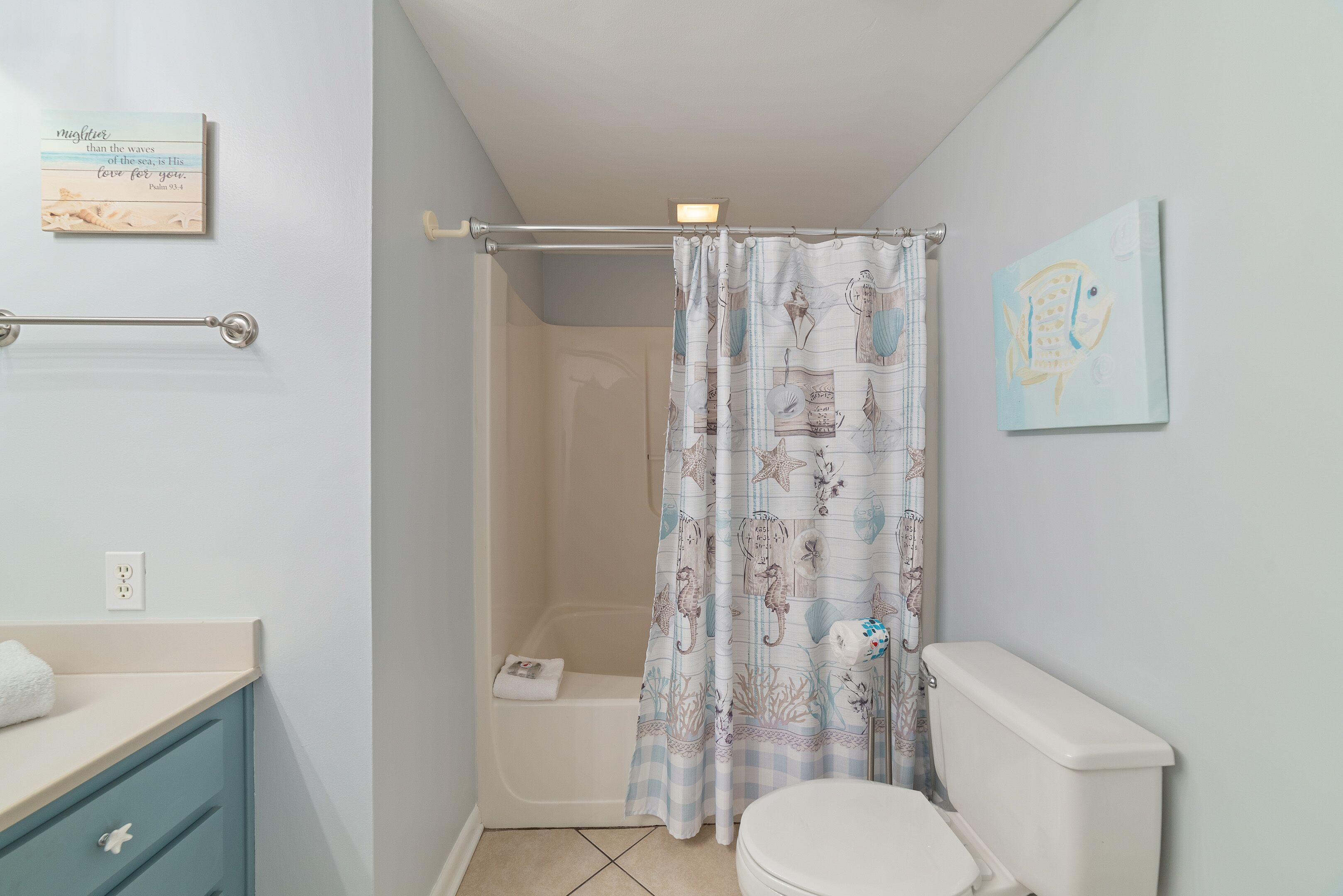 A bathroom with a shower curtain, a toilet, a sink with a towel, and a wall-mounted light fixture.