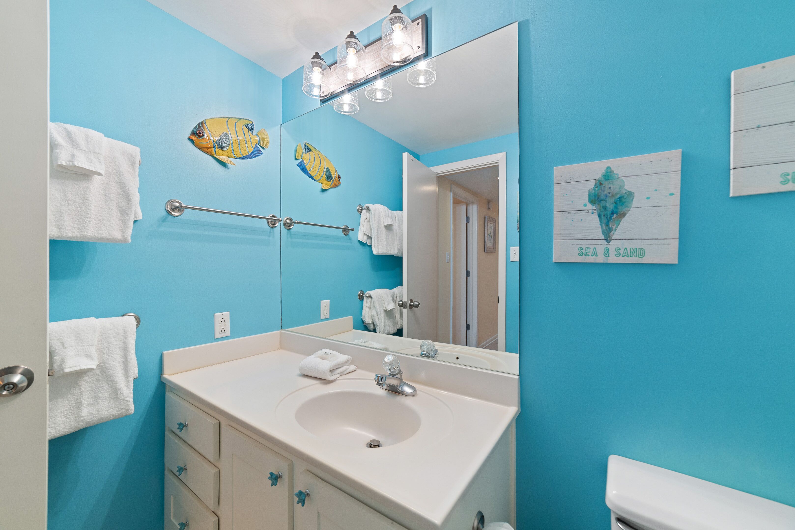 A bathroom with a blue wall, white sink, and two fish decorations.