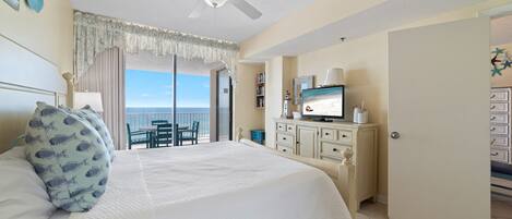 A bedroom with a bed, a television, a dresser, and a view of the ocean.