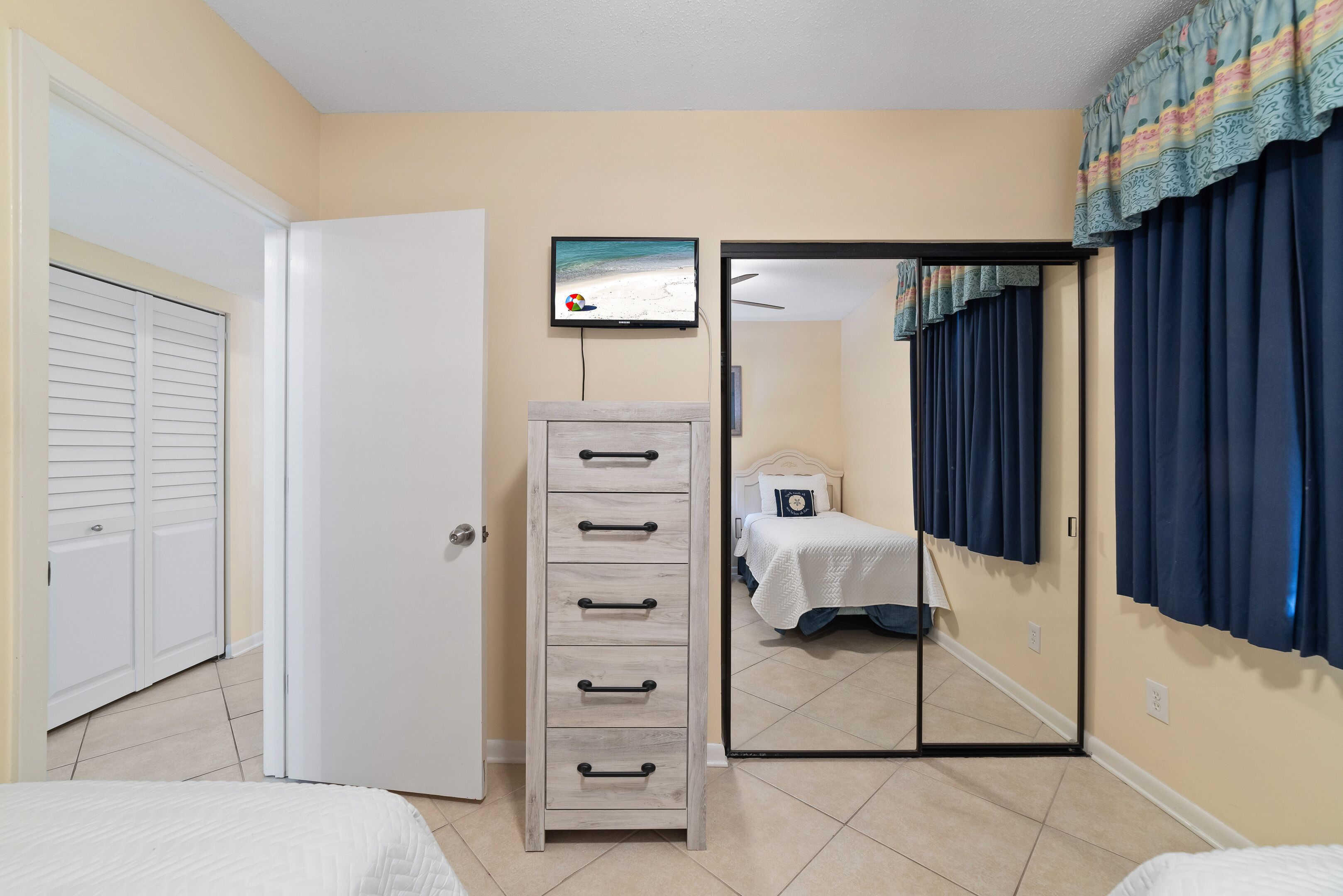 A bedroom with a bed, a dresser, a television, and a sliding door leading to another room.