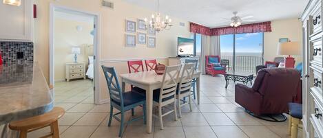 A dining area with a table and chairs, a chandelier, and a view of the ocean through a window.