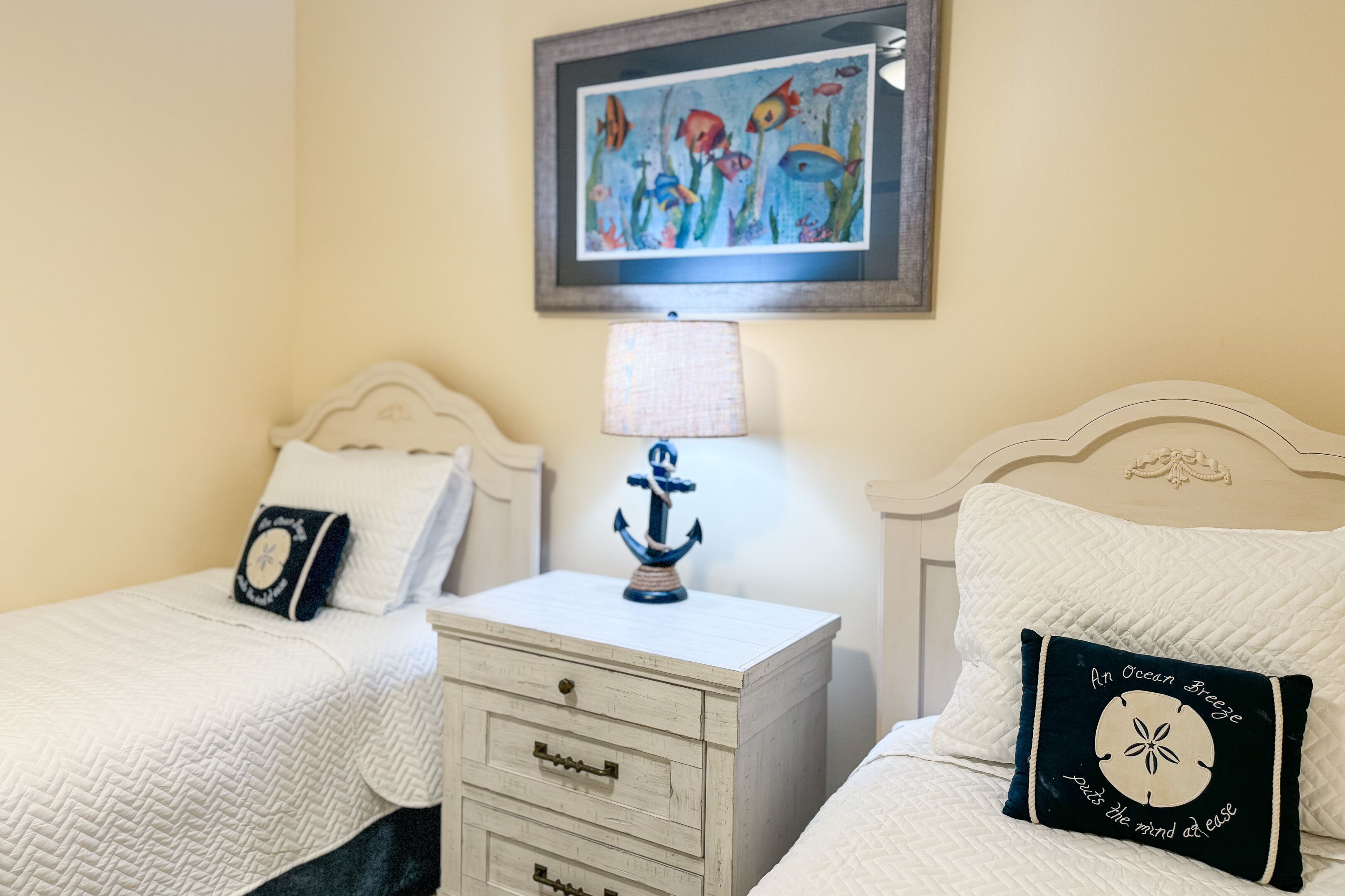A bedroom with two beds, a nightstand with a lamp, and a framed picture on the wall.