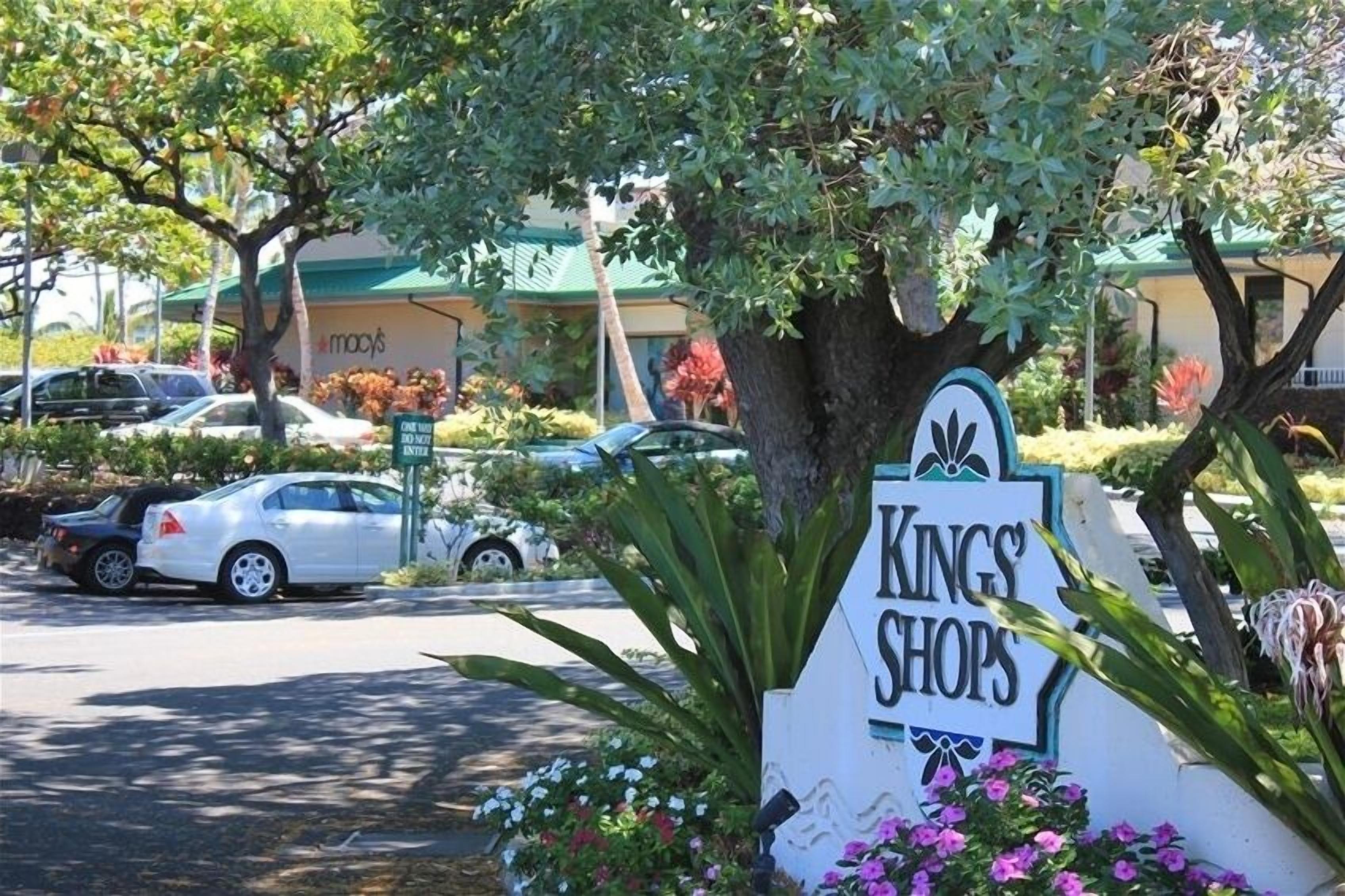 Een bord met 'Kings Shops', met een boom en bloemen op de voorgrond.