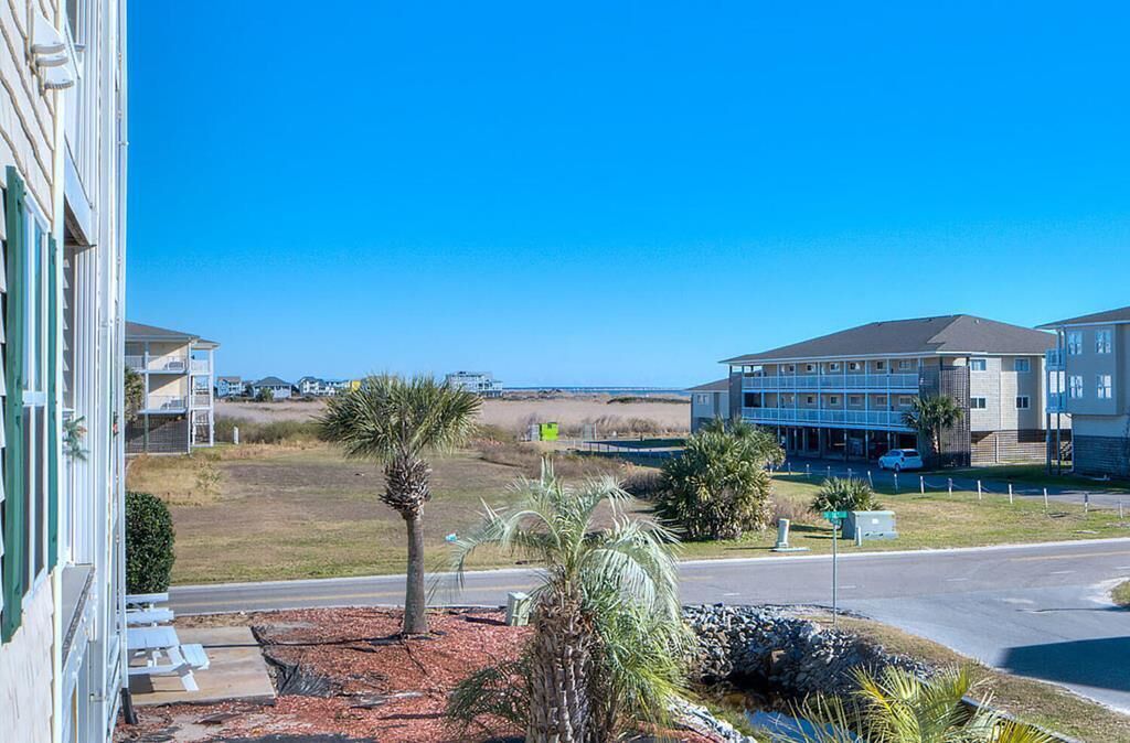 A residential area with a road, a building with a balcony, and a clear blue sky.