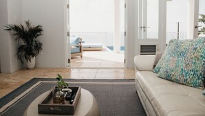 Een moderne woonkamer met een witte bank, een bijzettafeltje met een plant en uitzicht op een balkon met een stoel.