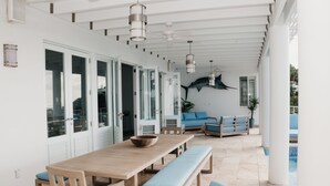 Een ruim terras met een houten tafel en banken, een zwembad en een blauwe bank.