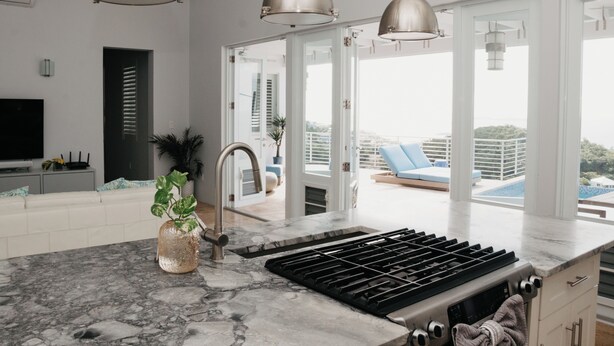 Een moderne keuken met een marmeren aanrecht, een roestvrijstalen spoelbak en hangende verlichtingsarmaturen.