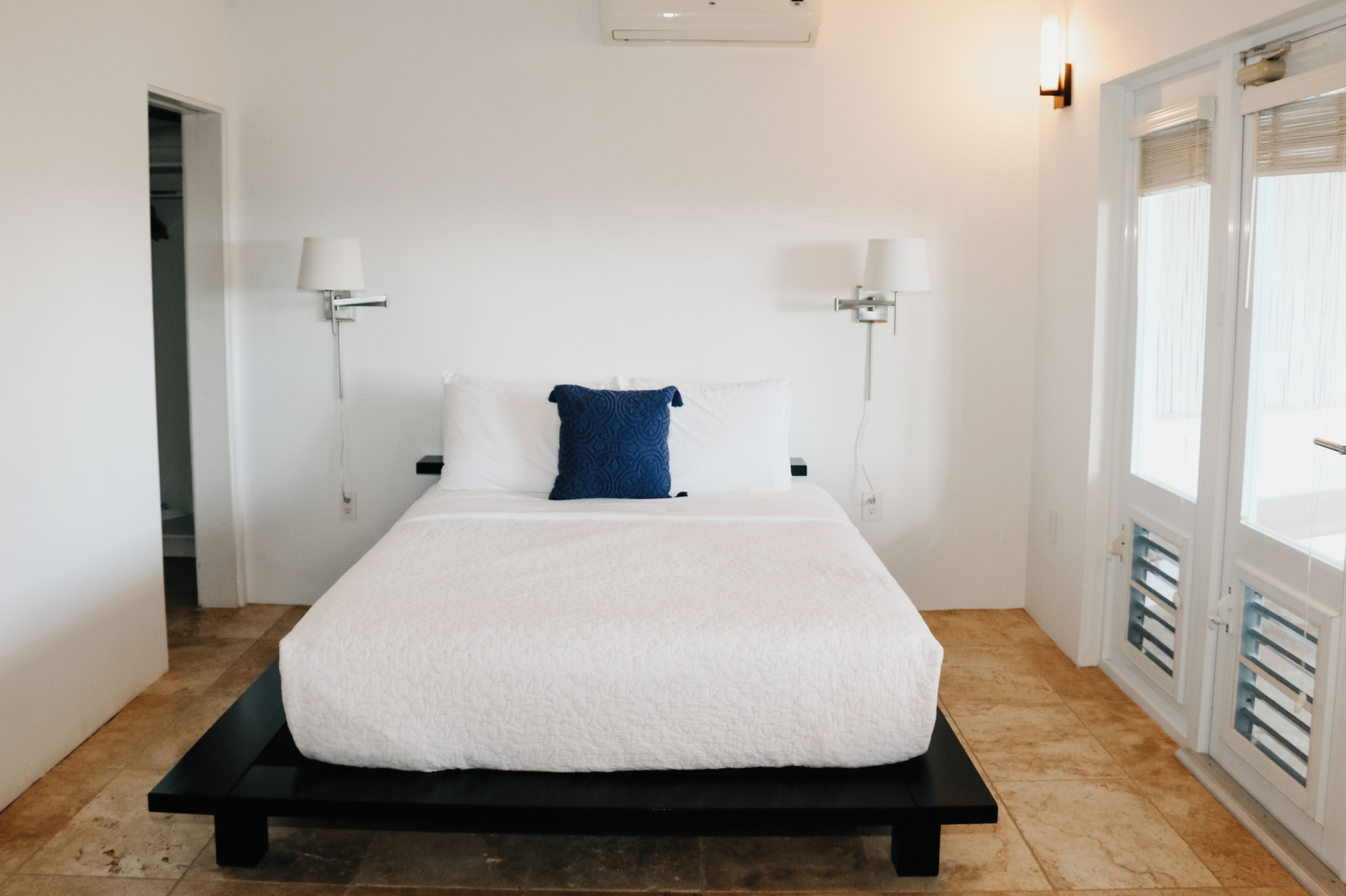 A modern bedroom with a large bed, white walls, and a door leading to a balcony.