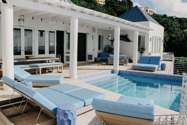Zona junto a la piscina con sillones de descanso, una mesa de comedor y un porche cubierto.