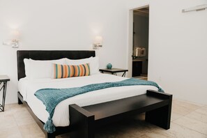 Un dormitorio moderno con cabecera negra, ropa de cama blanca, una manta color turquesa y dos lámparas de noche.
