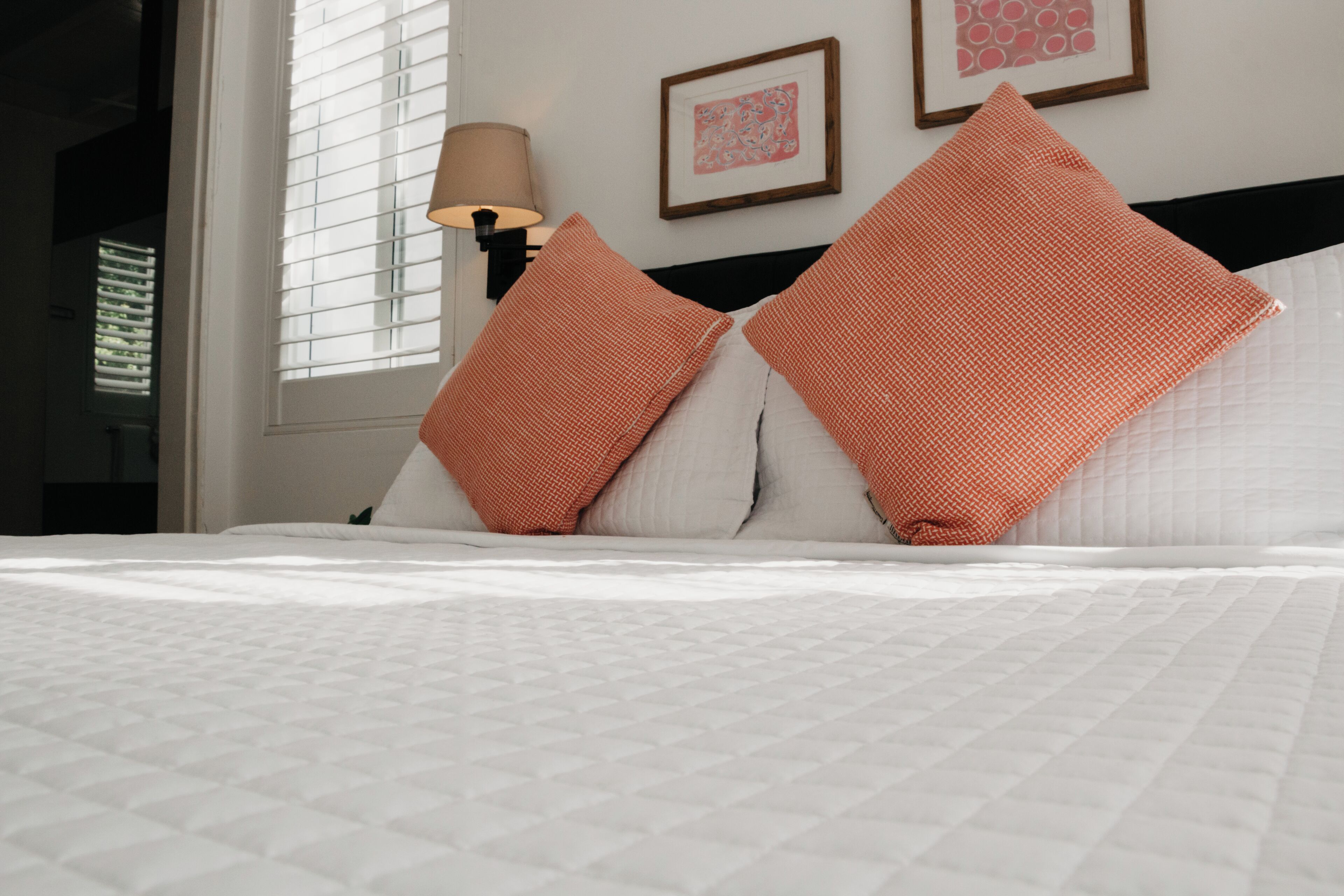 A neatly made bed with white bedding and two orange pillows.