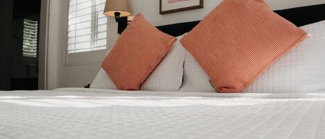 A neatly made bed with white bedding and two orange pillows.