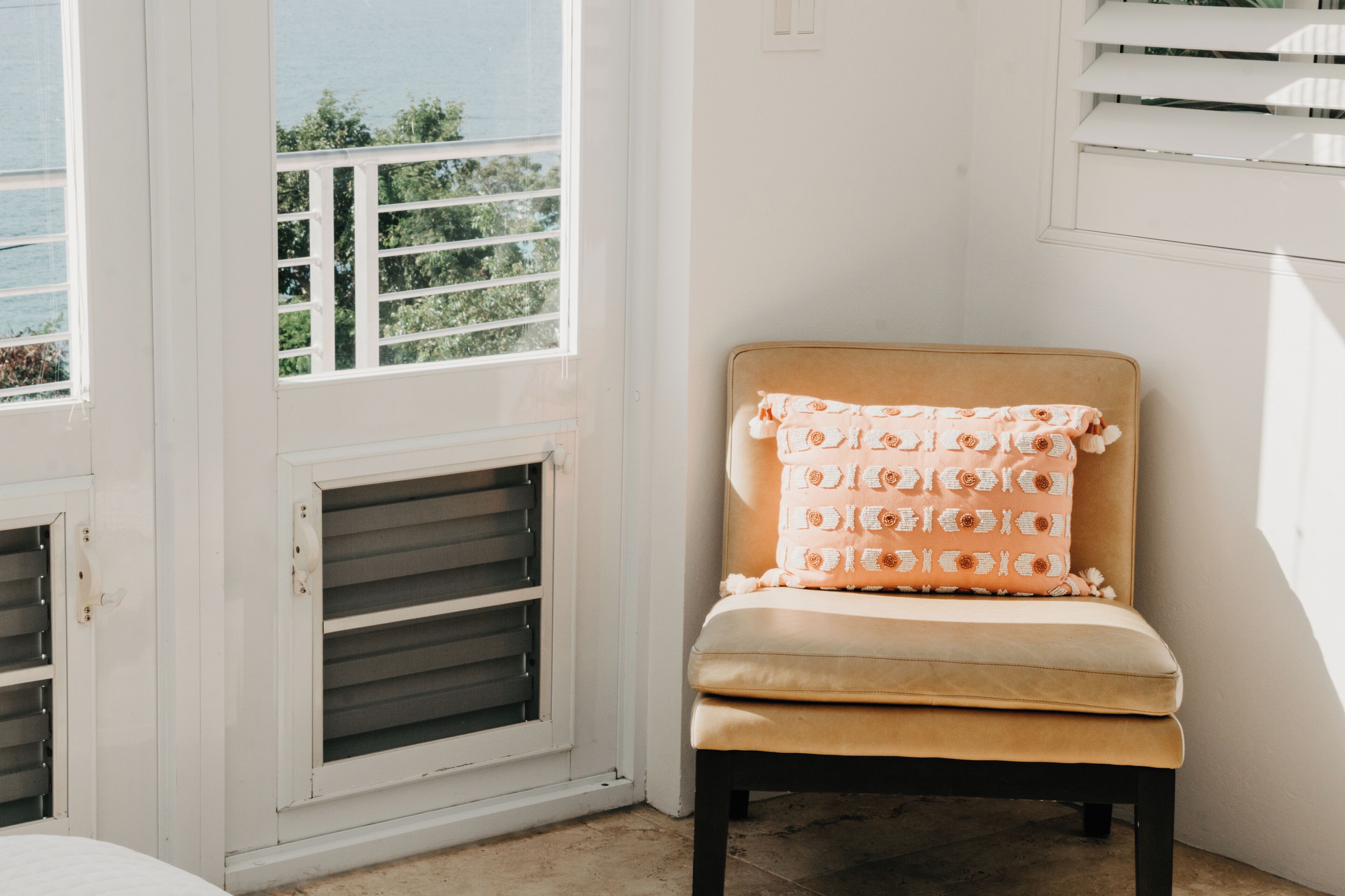 Une pièce avec une fenêtre, une chaise dotée d’un coussin à motifs et une vue sur la verdure à l’extérieur.